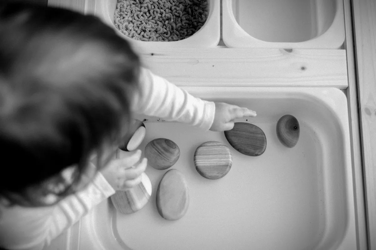 A mother resting her hand on a stack of smooth stones in soft black and white light